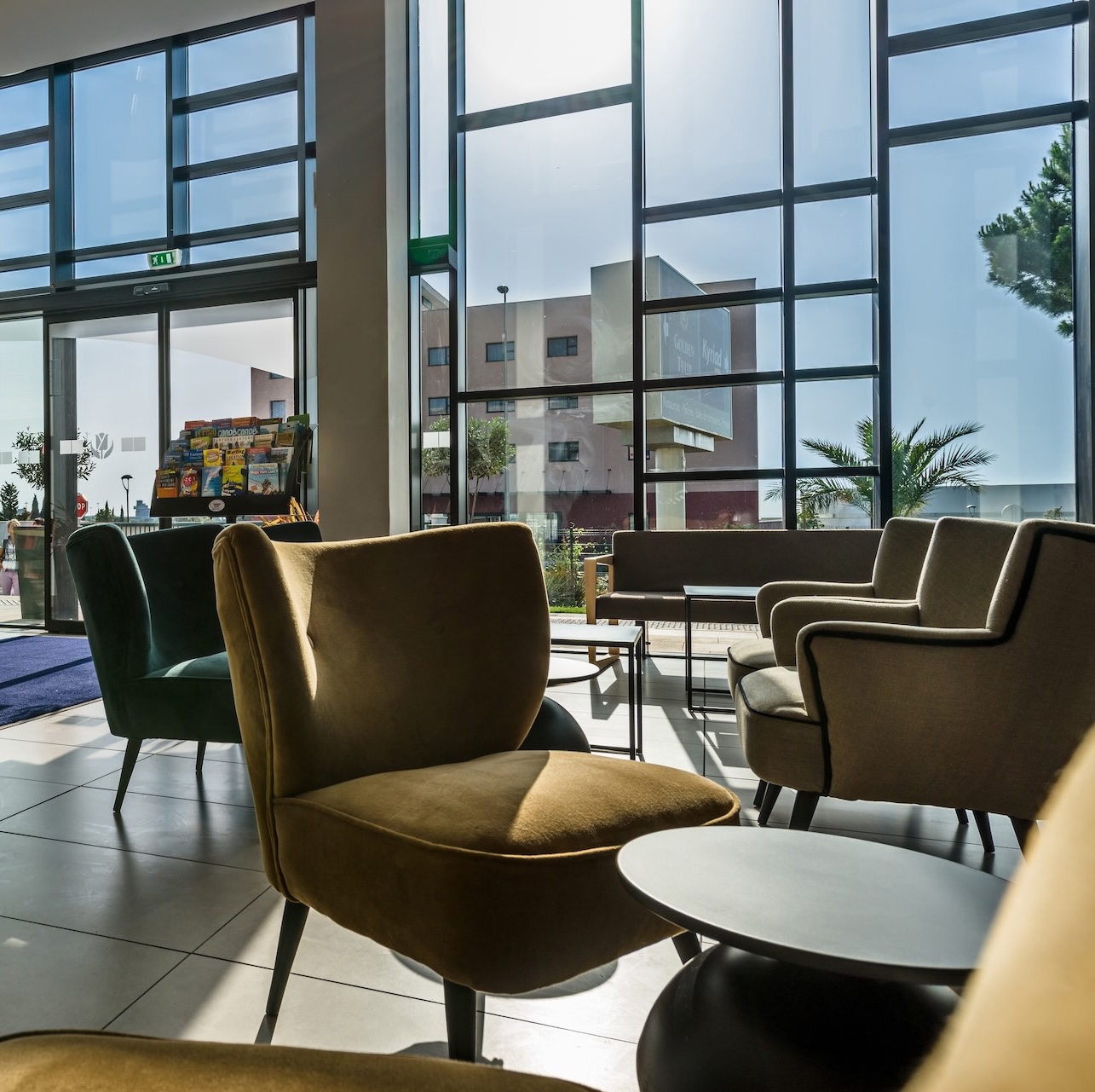 salon spacieux et lumineux avec de grands fauteuils, des tables basses, de grandes fenêtres et vue sur la rue extérieure en journée.